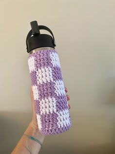 a hand holding a purple and white crocheted water bottle cover