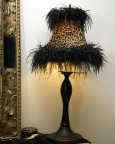 a lamp with a leopard print shade on it next to a mirror and a gold frame