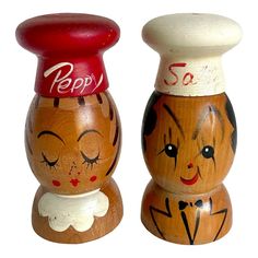 two wooden salt and pepper shakers with faces painted on the top one has a red cap