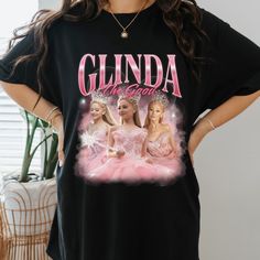 "Vintage 90s bootleg t-shirt featuring Ariana Grande as Glinda from Wicked. This unique design showcases a whimsical illustration of Glinda with vibrant colors and playful text, perfect for musical theater fans and collectors. Ideal for casual wear or as a standout piece in any wardrobe. Shop now for a touch of Broadway nostalgia! Glinda Popular, Wicked Ariana Grande, Ariana Grande Vintage, Glinda Wicked, Wicked Glinda, Glinda The Good, Merch Shirt, Glinda The Good Witch