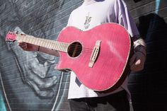 a man holding a pink guitar in front of a wall