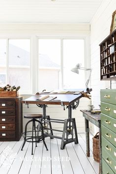 an old fashioned desk and chair in a room with white walls, wooden floors and large windows