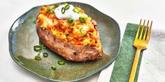 a baked potato topped with cheese and green onions on a plate next to a fork