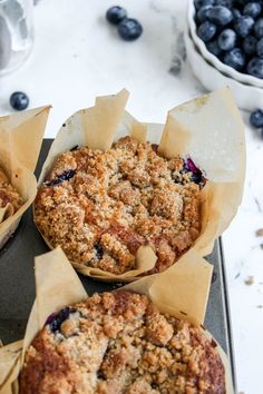 blueberry crumb muffins sitting on top of a baking pan next to fresh blueberries