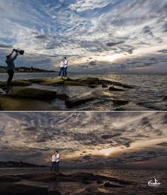 two people are standing on rocks near the ocean and one person is holding a camera