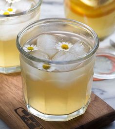 two glasses filled with lemonade and daisies on top of a wooden cutting board