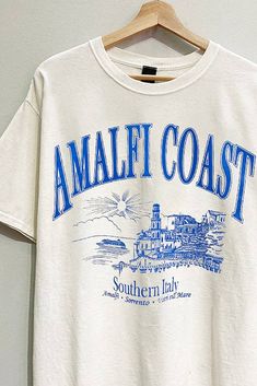 BACK IN STOCK! Embrace the coastal vibes this summer with our Amalfi Coast Graphic Tee. Crafted from premium washed cotton fabric, this tee offers a soft, lived-in feel that you'll love to wear all season long. The oversized fit ensures maximum comfort and style, making it a versatile addition to your summer wardrobe. The vibrant blue text pops against the fabric, bringing a touch of the Mediterranean to your everyday look. Perfect for pairing with denim shorts or a skort, this tee effortlessly Text Graphic Tee, Relaxed Acid Wash Tops For Summer, Oversized Casual T-shirt For Beach Season, Comfortable Text Print Tops For Summer, Casual Crew Neck T-shirt For Vacation, Comfortable Summer T-shirt With Letter Print, Comfortable Graphic Print Summer Top, Comfortable Summer Tops With Graphic Print, Comfortable Letter Print T-shirt For Summer