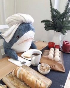 a stuffed shark with a chef's hat on sitting at a table next to bread and coffee