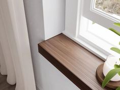 a white vase sitting on top of a wooden shelf next to a window