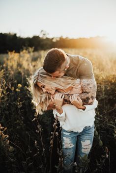 a man holding a woman in his arms while standing in tall grass with the sun behind him