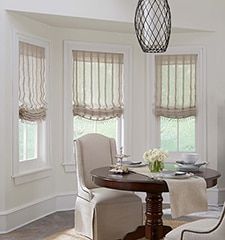 a dinning room table and chairs in front of two windows with roman shades on them