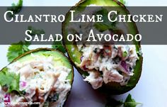 an avocado filled with chicken salad sitting on top of a white plate next to cilantro