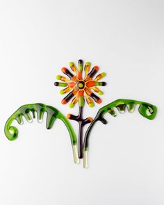 a colorful flower made out of glass sitting on top of a white surface with green stems