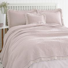 a bed with pink comforter and pillows on top of it in a white room