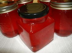 four jars with lids are lined up on a white tablecloth and one is filled with red liquid