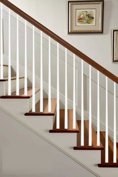 a stair case with white railing and wood handrails in a home setting, along with framed pictures on the wall