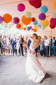 a bride and groom sharing their first dance under colorful paper lanterns at the end of an outdoor wedding reception