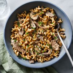 a blue bowl filled with pasta and meat on top of a white marble countertop