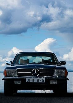 a black car parked on the side of a road next to some water and clouds