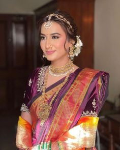 a woman in a pink and gold saree with jewelry on her neck, smiling at the camera