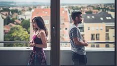 a man and woman standing next to each other on a balcony looking out at the city