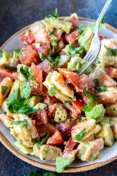 a salad with shrimp, avocado and tomatoes in a bowl on a table