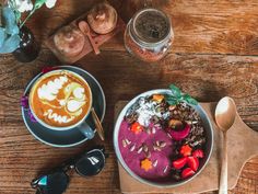 two bowls of food on a wooden table with spoons and glasses next to it