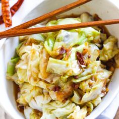 a white bowl filled with food next to chopsticks on top of a table