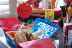 the lunch box is full of school supplies and has an apple shaped sign on it