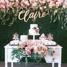 a table topped with lots of cakes and desserts next to a flower covered wall