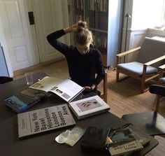 a woman sitting at a table with several books on top of it in front of her