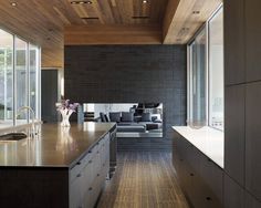 a modern kitchen with wood floors and black brick wall behind the countertop, along with large windows