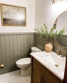 a white toilet sitting next to a bathroom sink under a round mirror with a plant in it