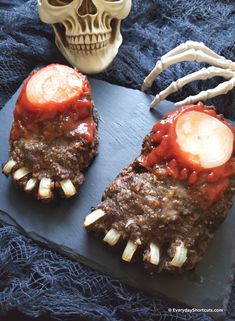 two meatloafs with red sauce and fake teeth on a black slate board