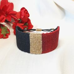 a close up of a bracelet on a table with red flowers in the back ground