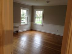 an empty room with hard wood flooring and two windows in the corner, looking into another room