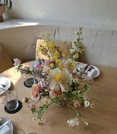 a vase filled with flowers sitting on top of a wooden table next to plates and utensils