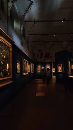 people looking at paintings on display in an art gallery with dark lighting from the ceiling