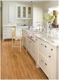 a large kitchen with white cabinets and wood flooring on the walls, along with a dining room table