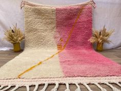 a pink and white rug with tassels on the floor next to two vases