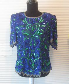 Stunning 1980s sequined beaded blouse. Royal blue and green. Made by Elegant Wear. Silk, lined. Has shoulder pads that can easily be cut out. Zigzag hems. Silver elongated beads at neckline and all edges. Zipper back. Great condition don't see any missing beads or sequins but cannot rule it out. Fits medium to large but please check your measurements. Bust 40" Length 24", 2 inches longer in back Shoulder to shoulder 16" FOR RETURNS YOU MUST MAIL BACK WITHIN 7 DAYS OF RECEIVING YOUR ORDER AND BUY Green Sequined Short Sleeve Tops, Green Tops For Evening Party Season, Green Sequined Party Blouse, Fitted Green Top For Holiday, Fitted Green Top For The Holiday Season, Fitted Blue Embellished Blouse, Green Sequined Blouse For Evening, Fitted Green Sequined Blouse, Green Embellished Festive Tops