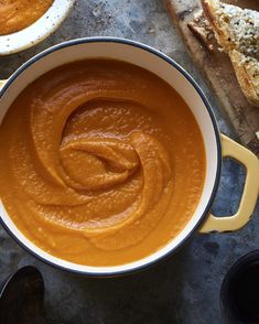 there is a bowl of soup on the table next to some bread and spoons