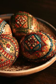 four decorated eggs in a bowl on a table