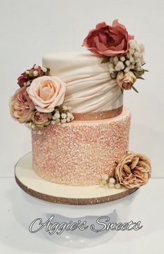 a three tiered cake decorated with flowers and glitters on a white tablecloth