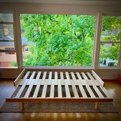 a wooden bed frame sitting in front of a window on top of a hard wood floor