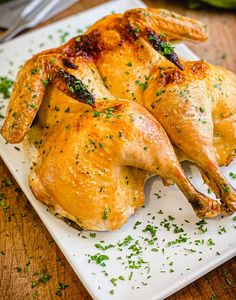 two roasted chickens on a white plate with parsley sprinkled around the edges