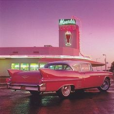 an old red car is parked in front of a drive - in restaurant with a tall neon sign