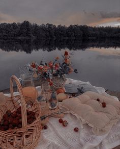 a picnic table is set up by the water with flowers and fruit in baskets on it