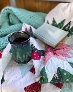 a green cup sitting on top of a bed next to a quilted blanket and book