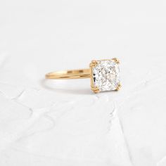 a yellow gold ring with a square cut diamond in the center on a white background